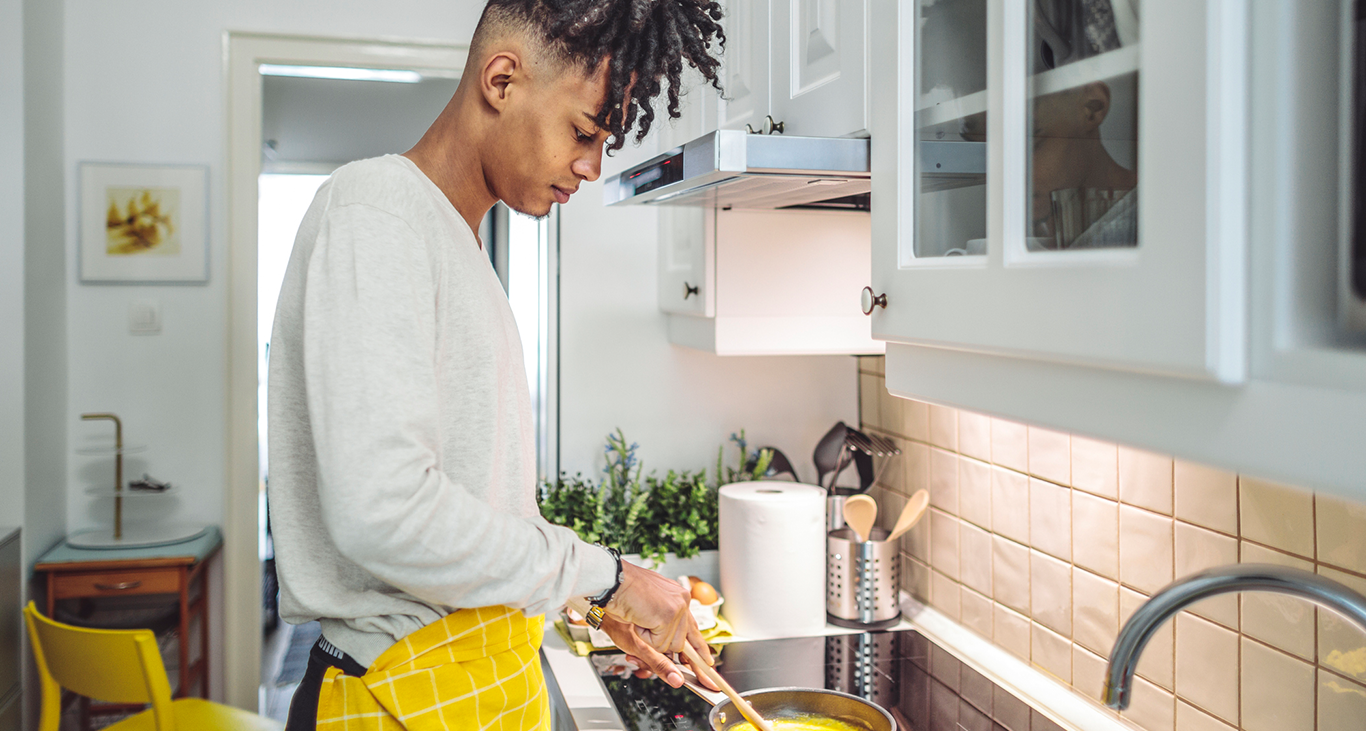 Young Black man practices young adult life skills by learning to cook