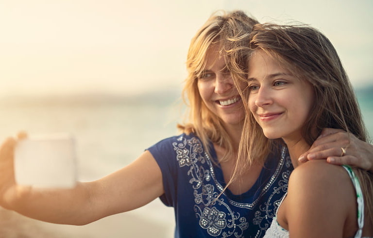 A mom and daughter taking a selfie together on a beach