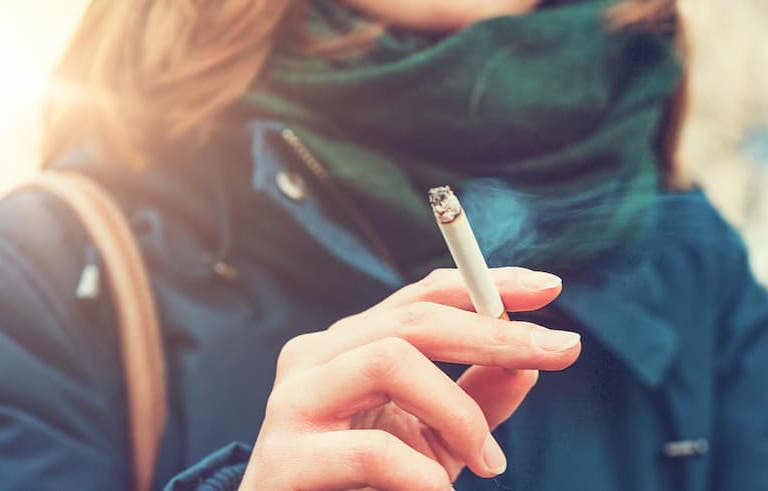 Closeup of cigarette being held by a young woman.